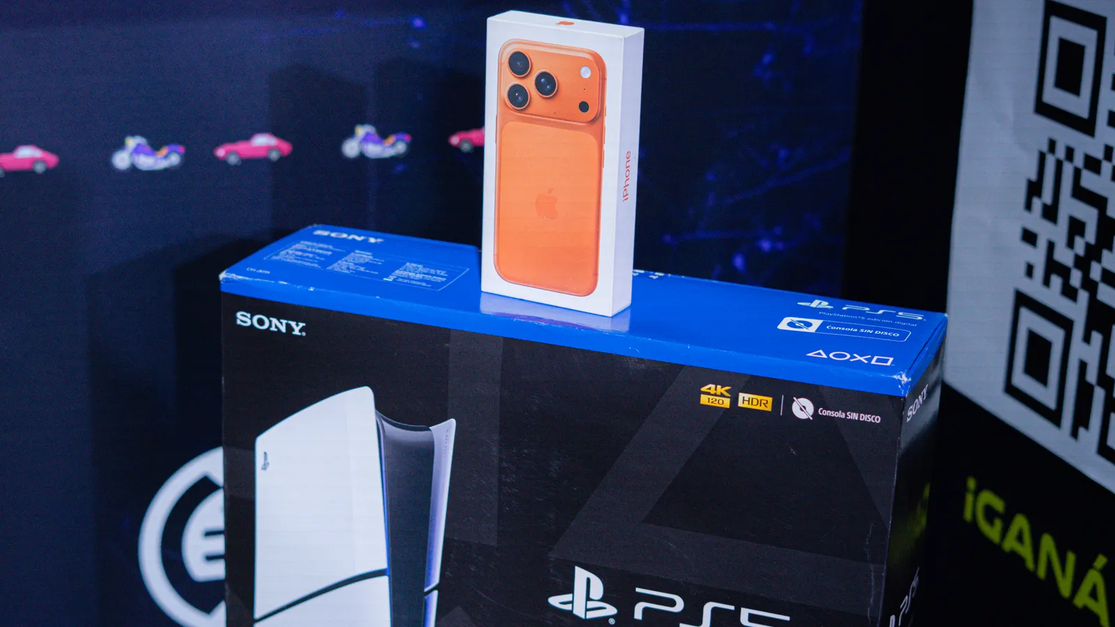 The orange iPhone 17 Pro box resting on the PlayStation 5 one, on the Eolax stand, beside the entry QR code.