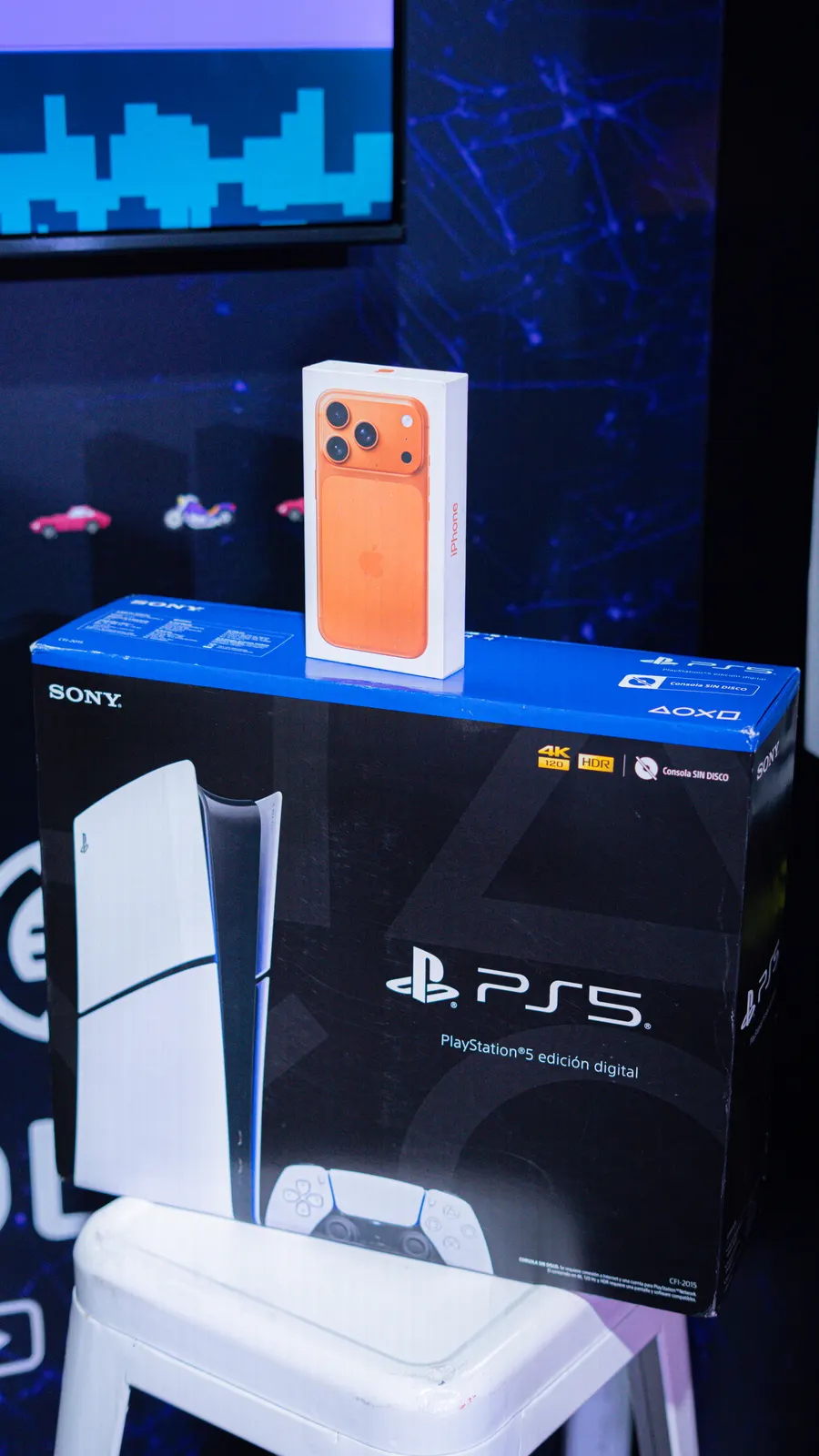 The stand's prizes: a PlayStation 5 Digital Edition box with an orange iPhone 17 Pro resting on top.