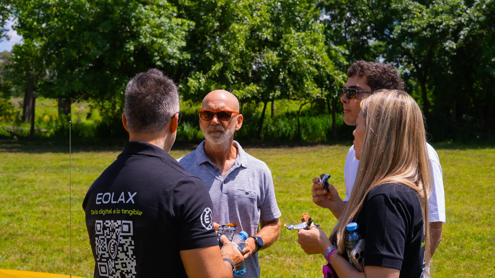 A team member, the Eolax QR code on the back of his shirt, talks with two guests on the grass.