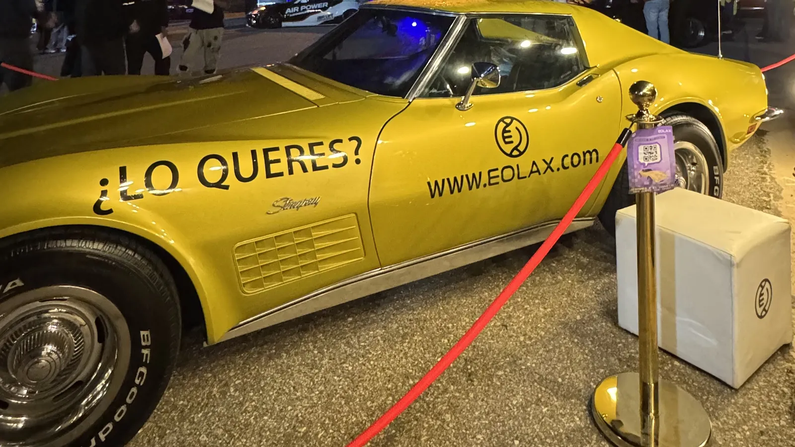 The gold Corvette Stingray behind the circuit's red rope at night, «¿LO QUERÉS? WWW.EOLAX.COM» on its door.