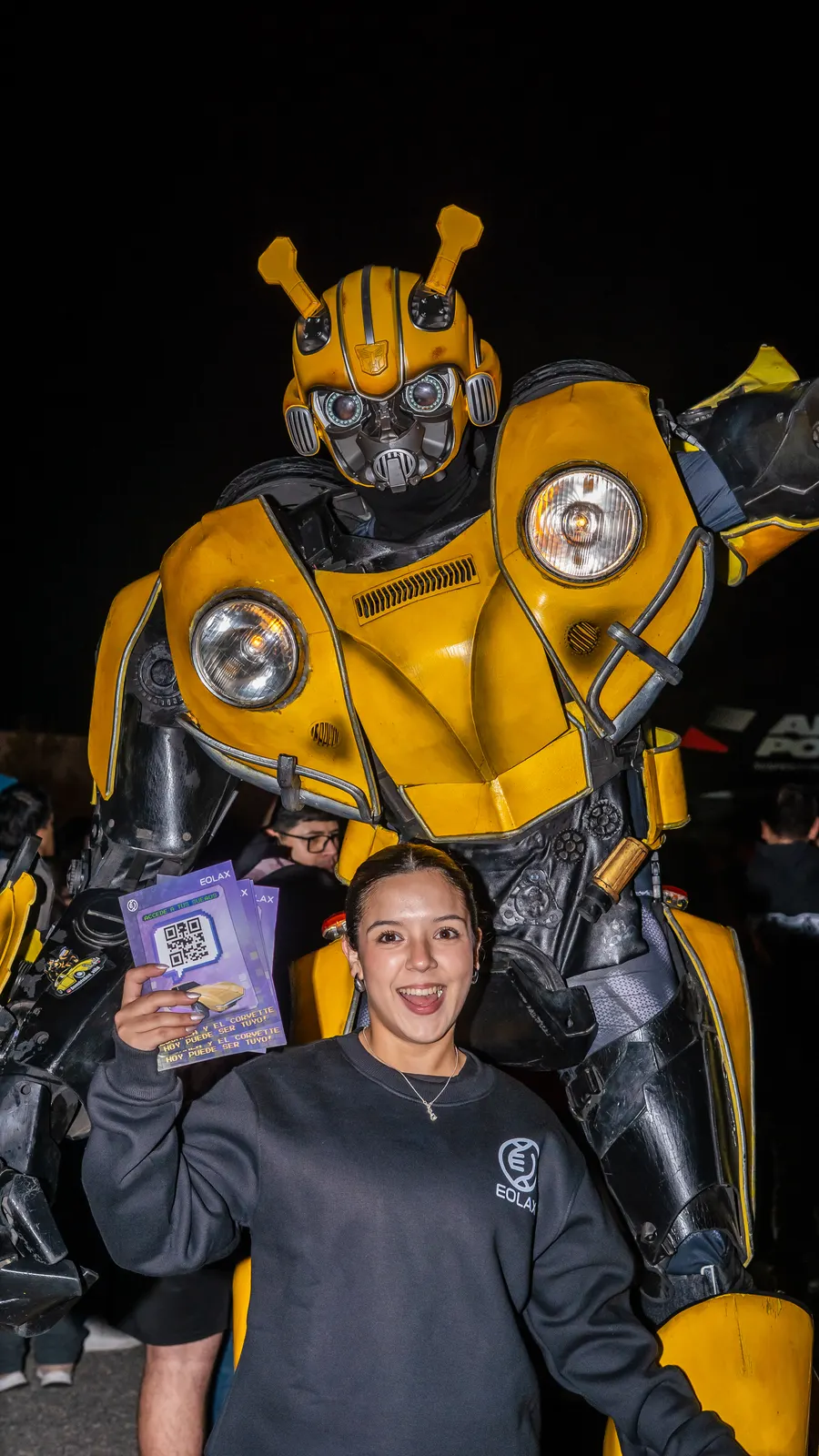 A guest shows her Eolax ticket in front of a giant Bumblebee figure at night.